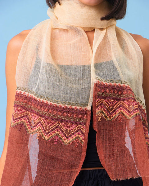 Woman wearing a patterned scarf against a blue background. scarf is najaf fabric and hand embroidered with palestinian embroidery by inaash association.