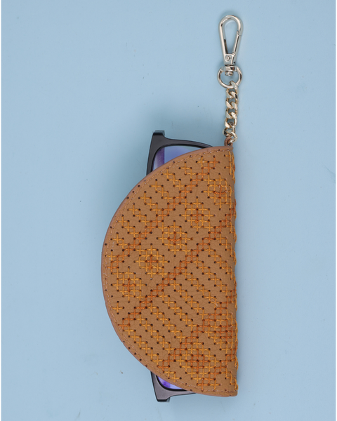 A tan woven half-moon style sunglasses case with a silver metal clasp and chain, holding a pair of sunglasses, on a light blue background.