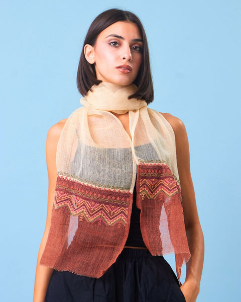 Woman wearing a patterned scarf against a blue background. scarf is najaf fabric and hand embroidered with palestinian embroidery by inaash association.
