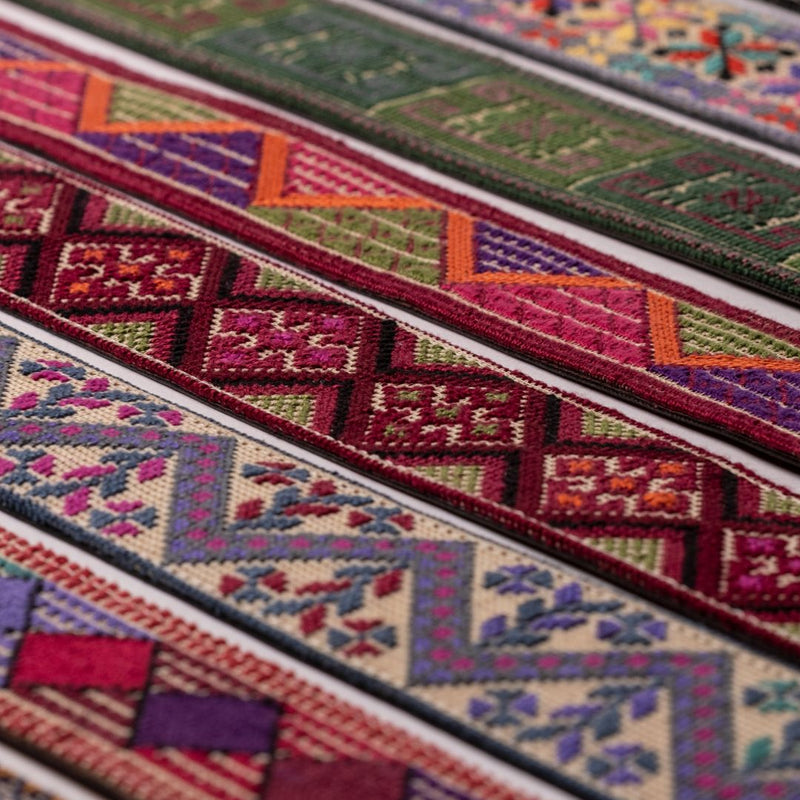 Close-up of multiple colorful embroidered textile bagstraps with geometric and floral patterns in red, green, purple, orange, blue, and cream.